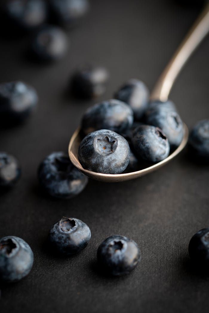 A close-up shot of fresh blueberries on a silver spoon, highlighting their natural texture and color.