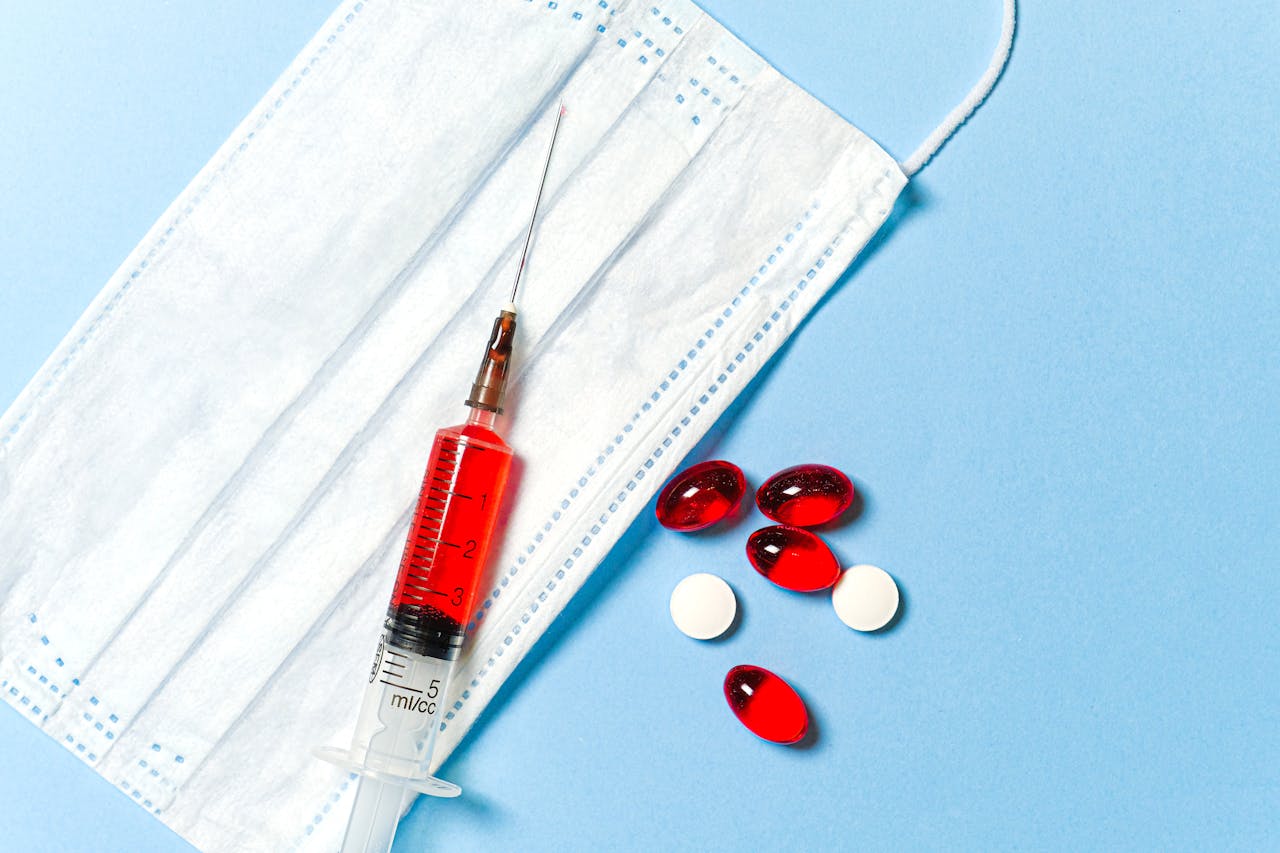 A syringe, face mask, and pills on a blue surface, symbolizing medical treatment.