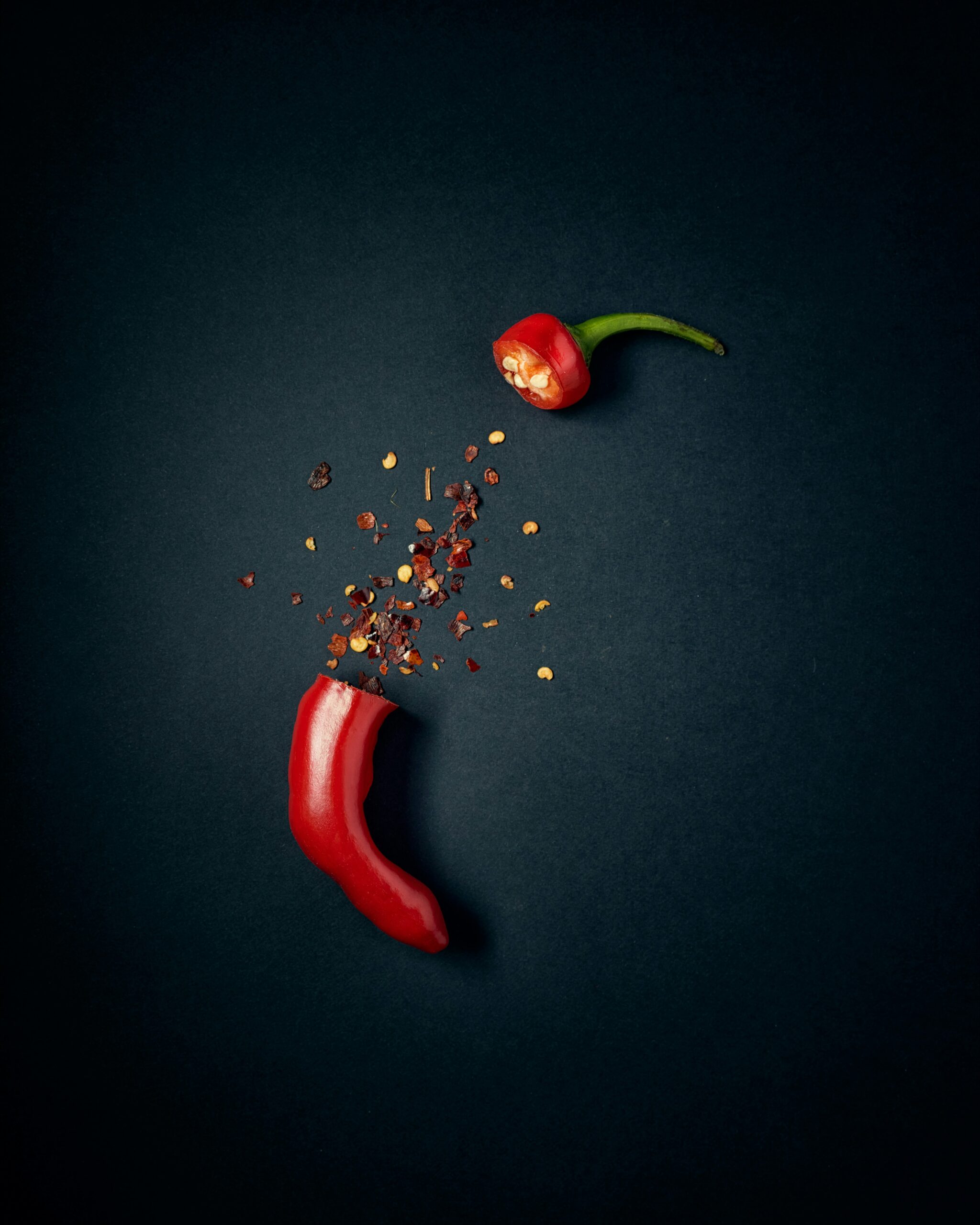A chili on a dark background spilling out chili flakes, this is symbolising Capsican longevity treatment myths from our List of Life Extension Techniques.