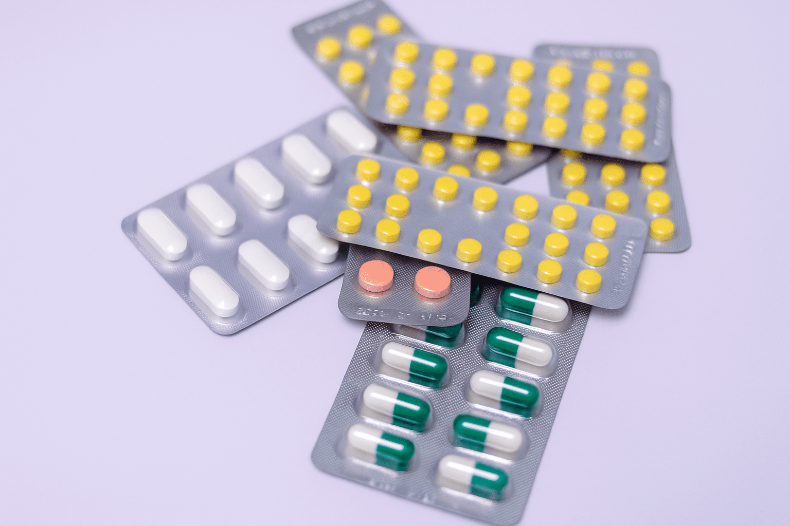 Blister packs of taurine supplements in various colors and shapes on a soft purple background.