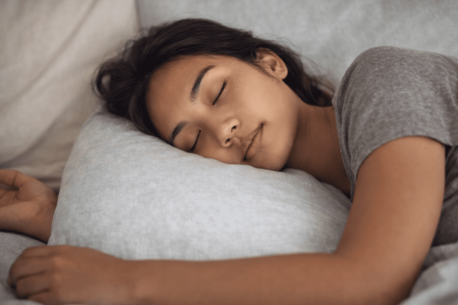 A woman sleeping peacefully on her side with her head on a pillow, representing deep, restorative sleep.